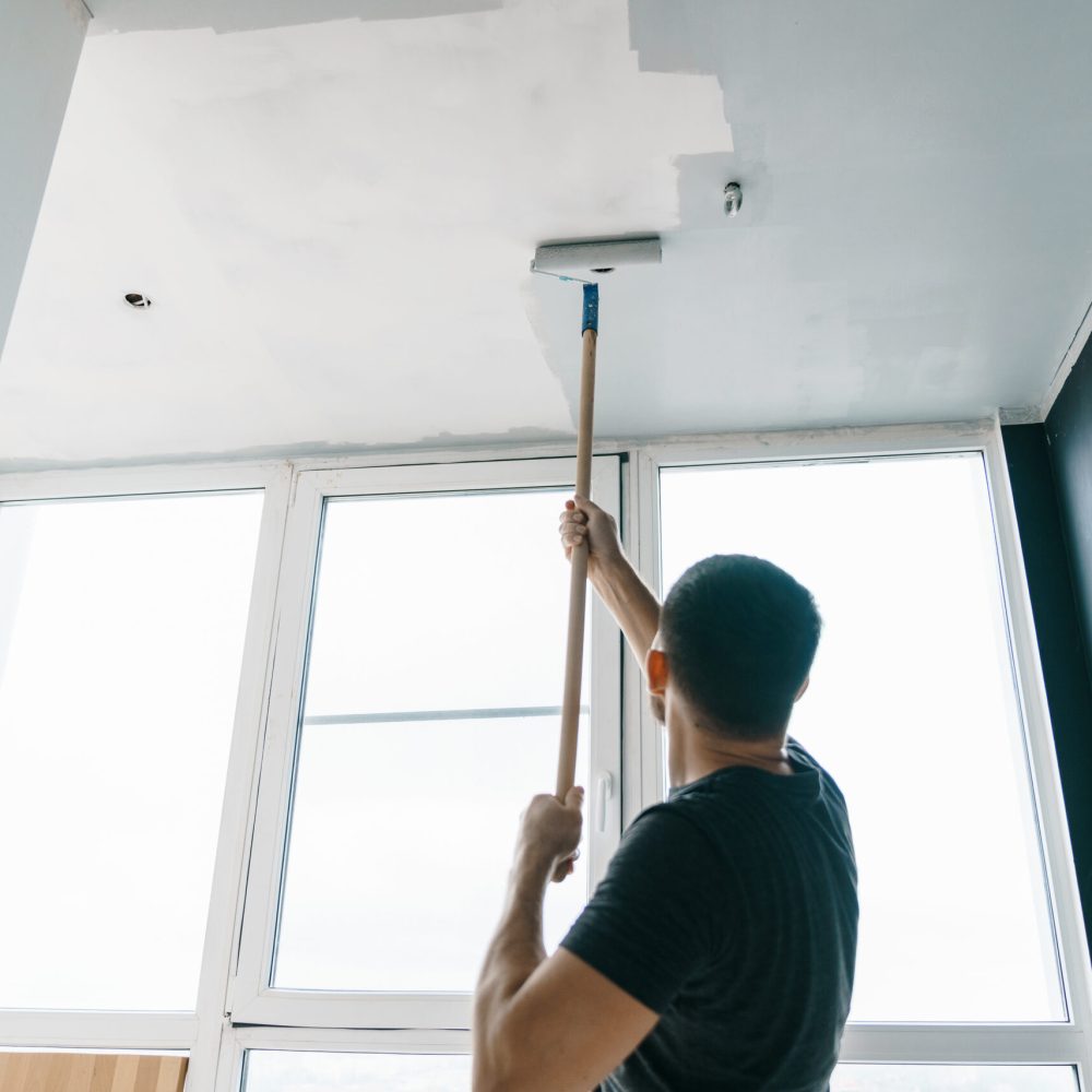 the man paints the walls and the ceiling in gray color, standing with his back to the camera. Focus on the roller. Painting and repair of the room.