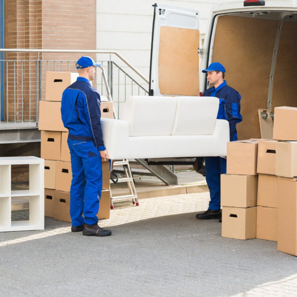 Full length of young male movers carrying sofa outside truck on street